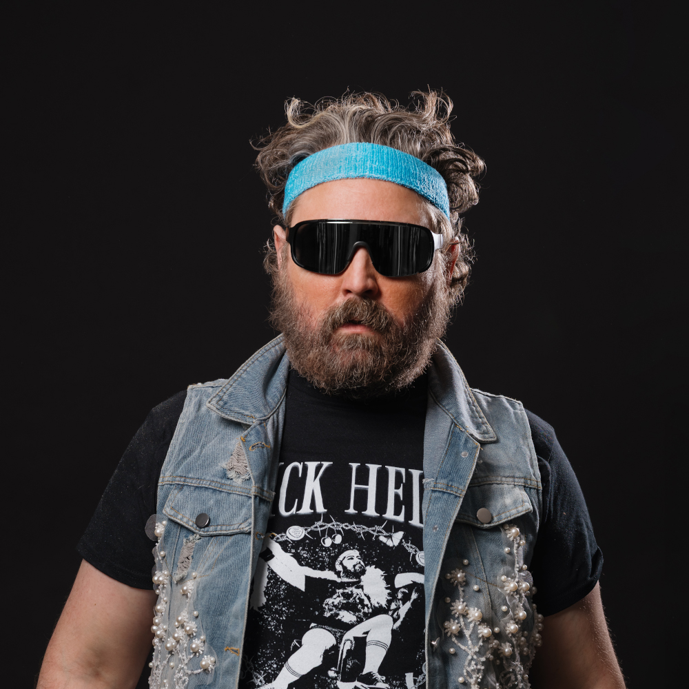 Photo of Nick Helm in a sleeveless denim jacket, headband and sunglasses